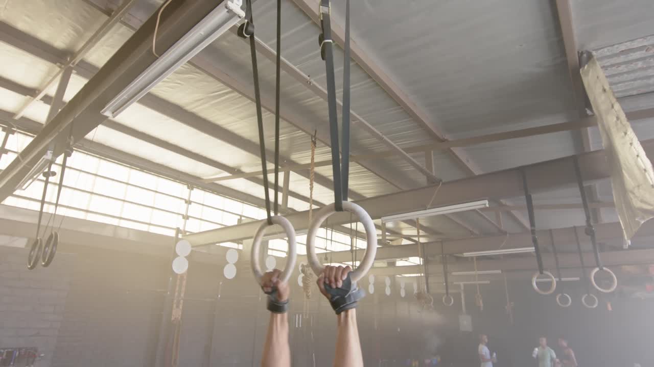 hombre biracial enfocado haciendo flexiones en los anillos del gimnasio en el gimnasio, en cámara lenta