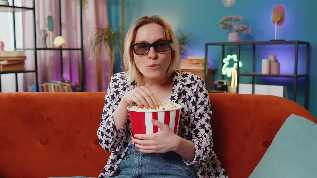 excitada mujer asombrada sentada en el sofá comiendo palomitas de maíz y viendo interesante serie de televisión juego de películas