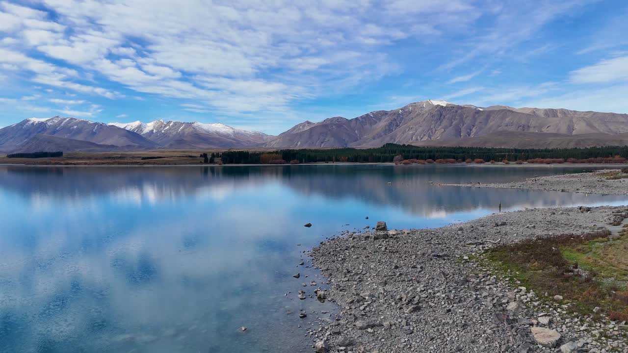 Drone footage captures Lake Tekapo's serene landscape, showcasing reflective waters and distant mountains under a vibrant sky