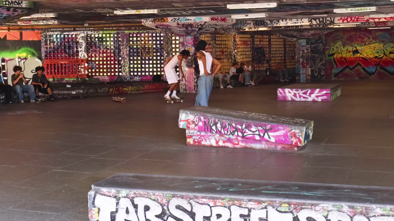 Skateboarders showcase tricks on ramps surrounded by colorful graffiti in an indoor skatepark.