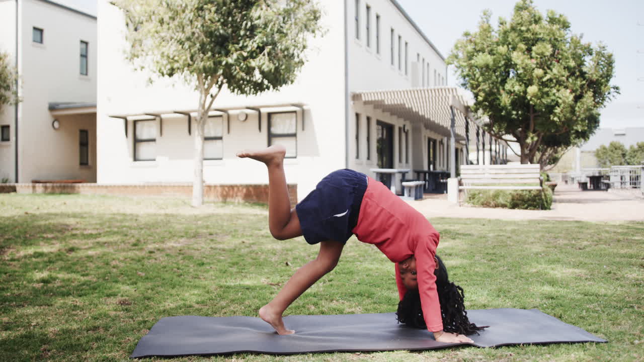 Young girl practicing yoga on mat outdoors at school, balancing with focus