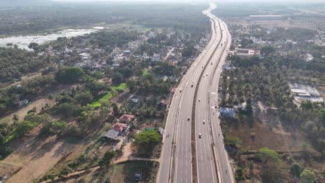 expansive aerial footage: a major highway in india. it traverses semi-urban areas with houses, green groves, and a prominent lake. great for infrastructure and rural growth narratives