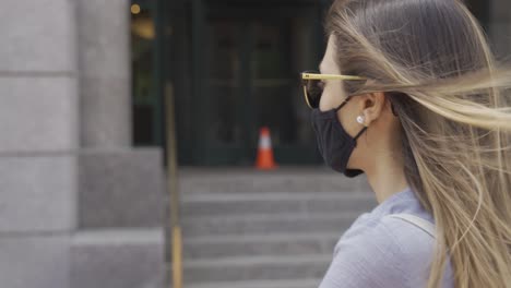 Wind-blowing-in-blond-woman-wearing-black-facemask-in-urban-setting-profile-shot