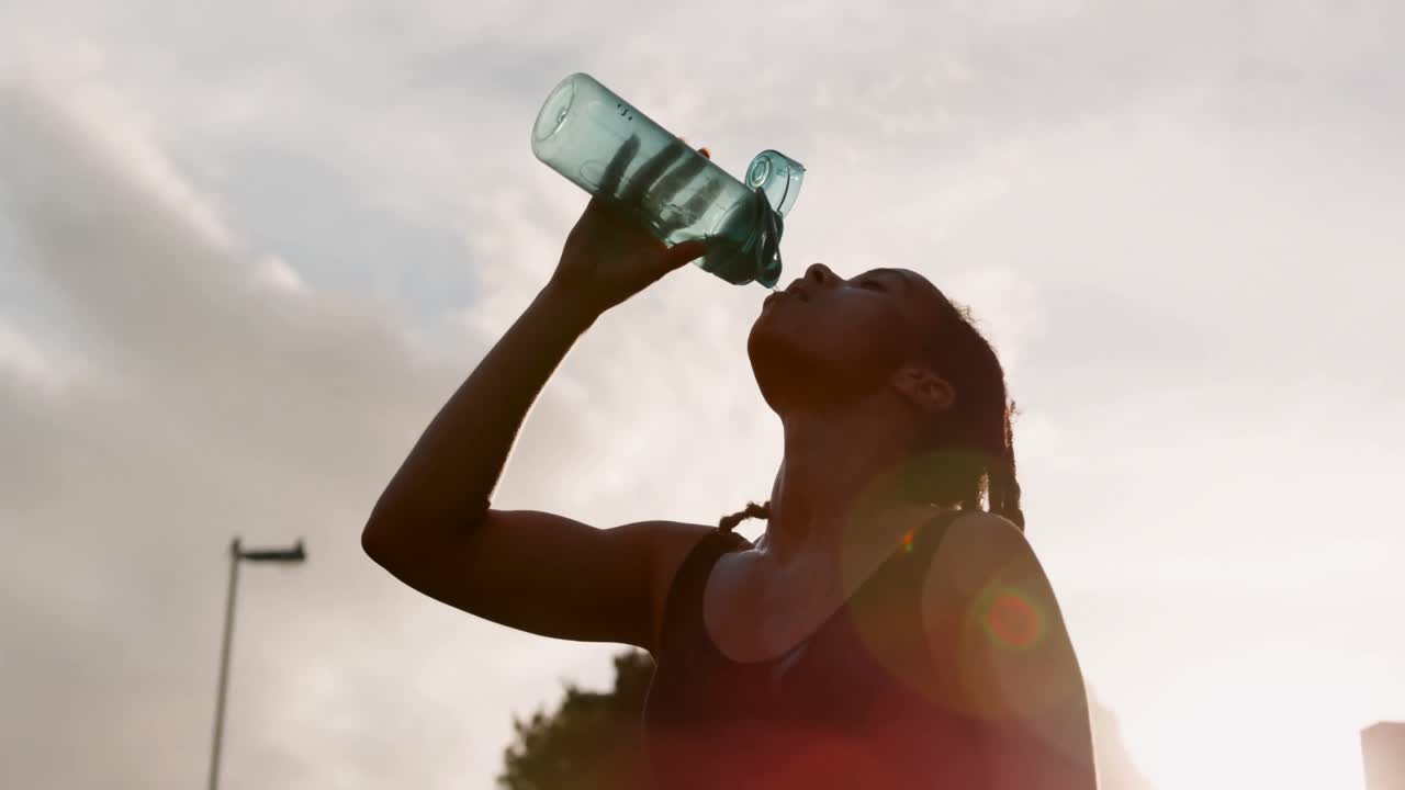 Low angle view of young African American woman drinking water in the city 4k