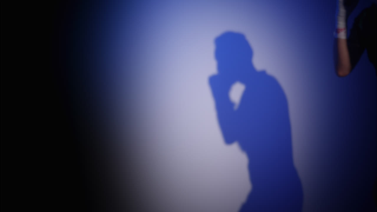 Ombra di un pugile che si allena e tira pugni su un muro blu