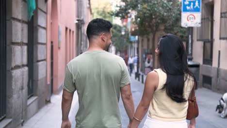 young couple holding hands and talking as the walk on sidewalk in city