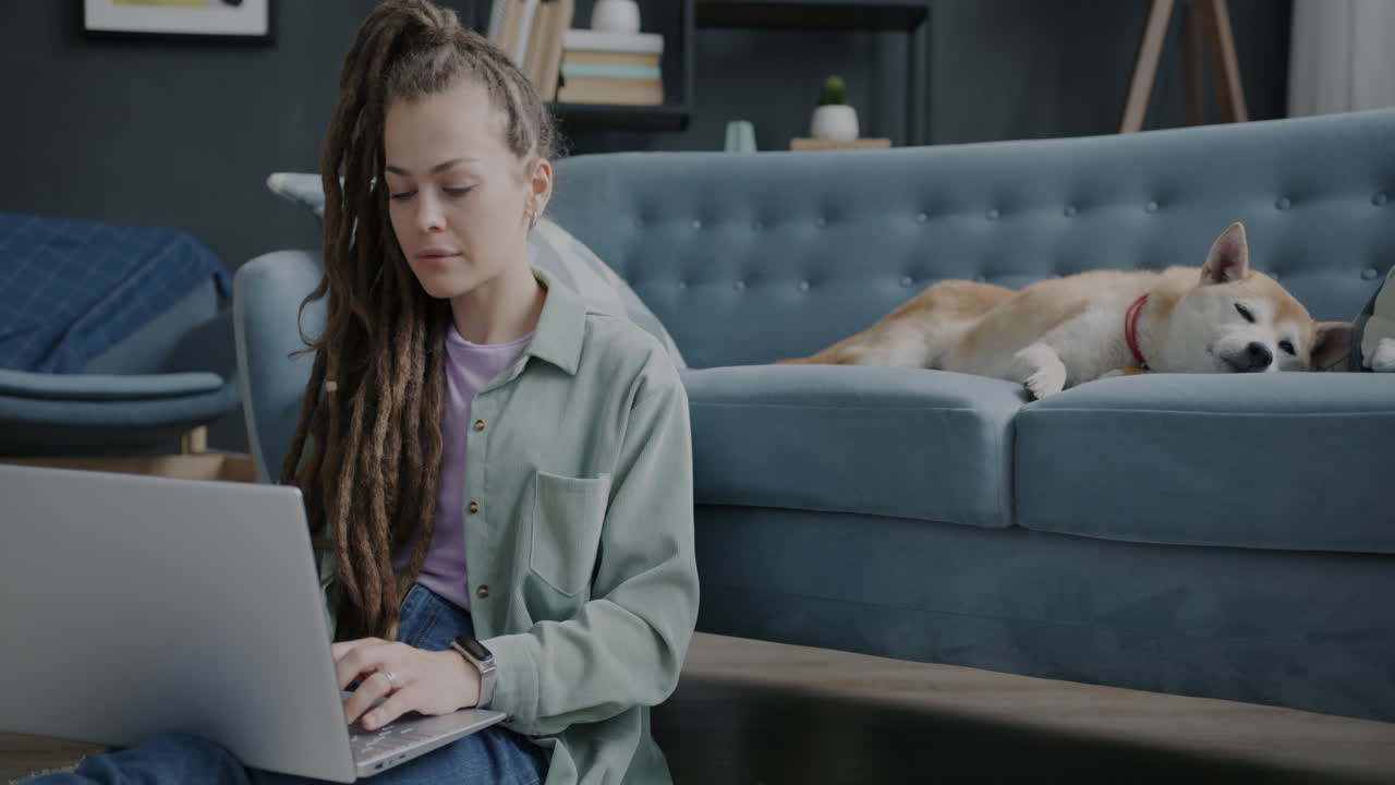 Woman working on laptop with dog resting on sofa