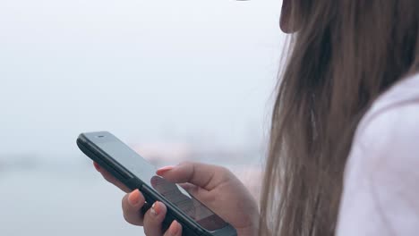 long haired brunette stands with phone against blurry sea