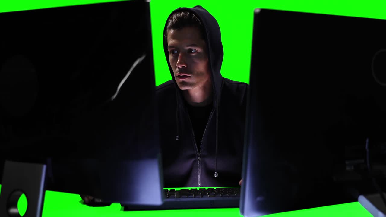 hacker usando dos computadoras con pantalla verde