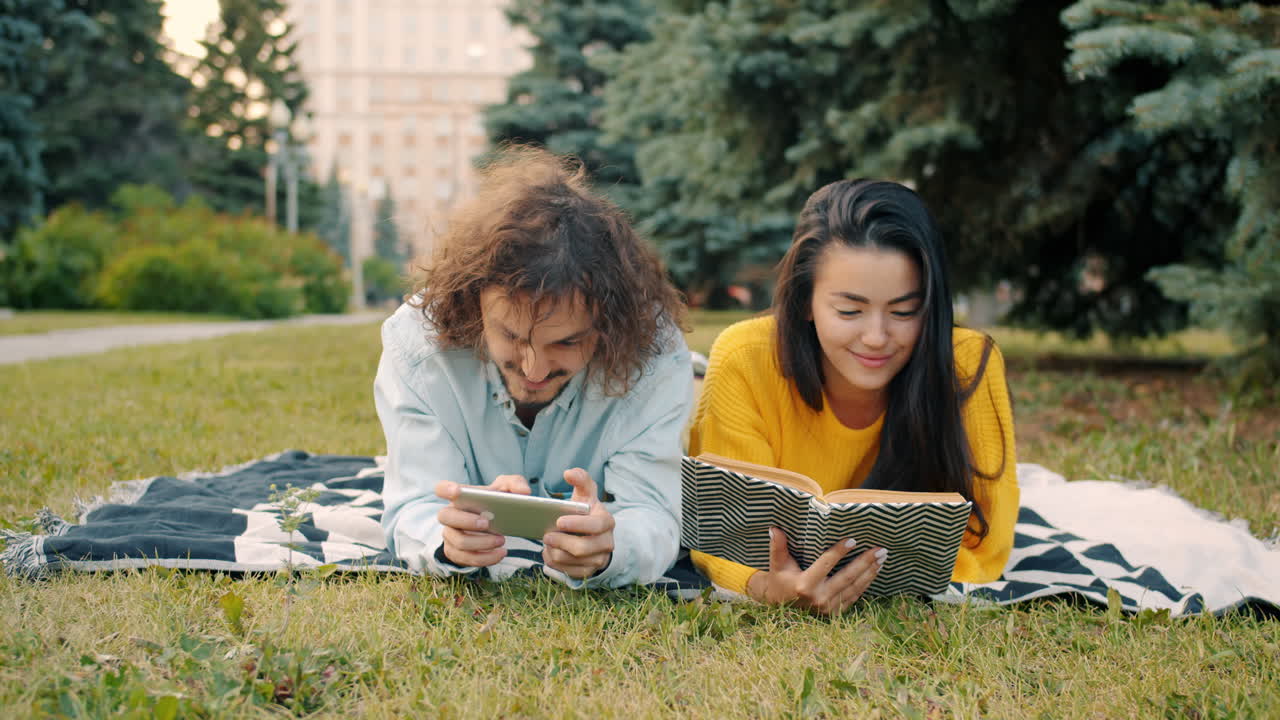 Pareja relajándose en el parque con libro y teléfono