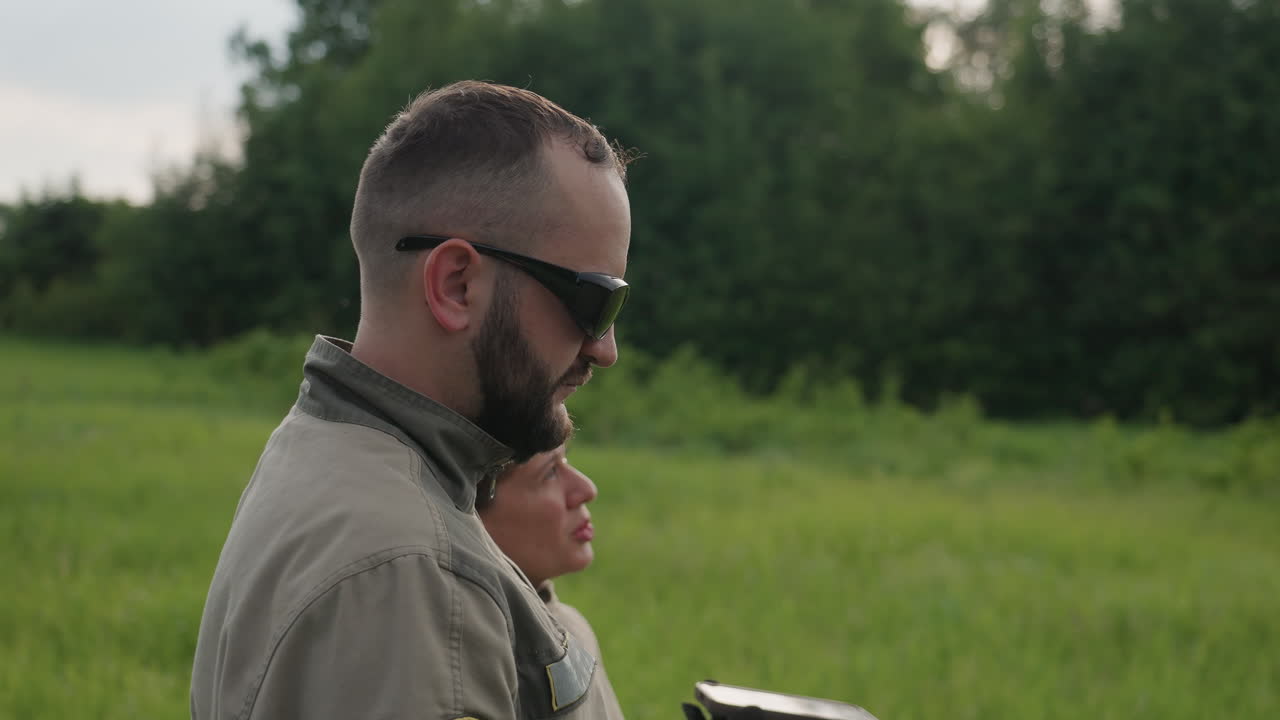 adult man and woman stand in verdant field gazing skyward through binoculars and pointing toward distant horizon while insects swarm overhead