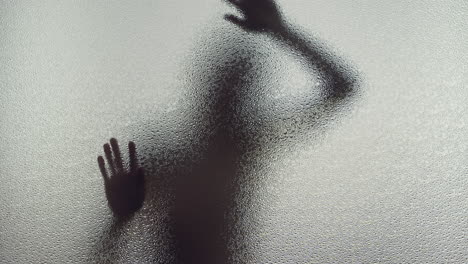 a female silhouette behind the frosted glass moves slowly
