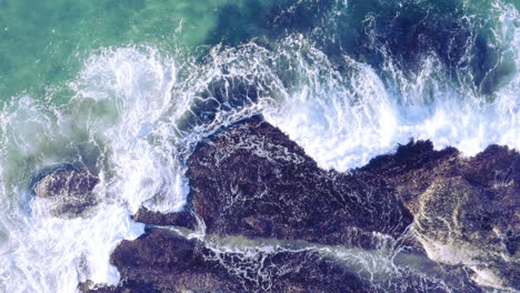 White-fringed-waves-crashing-in-from-top-of-screen-onto-sea-rocks-Tamarama-Beach-Sydney-Australia-POV-drone-directly-above