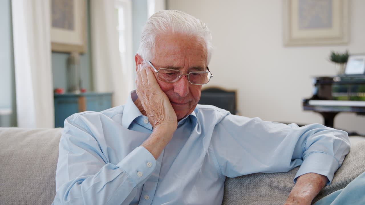 Senior Man Sitting On Sofa At Home Suffering From Depression