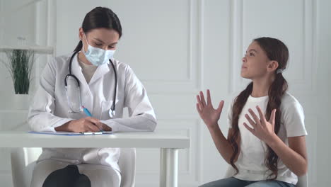 Young-pretty-female-doctor-with-a-face-mask-treating-a-little-girl-patient-in-her-office