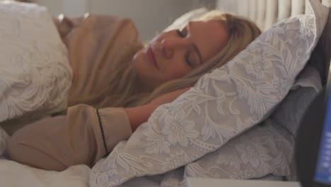 woman sleeping in bed with sleep data app running on mobile phone on bedside