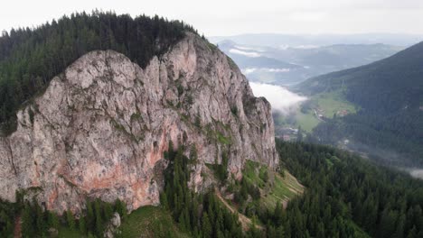 Enormous-rock-face-sticking-out-in-the-landscape,-surrounded-by-forests,-aerial