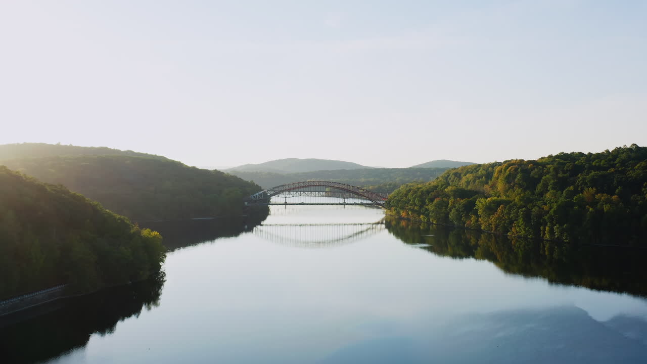 Drone fly-in capturing the peaceful New Croton Reservoir with the iconic bridge reflecting on the still waters. Framed by lush green hills in Westchester, NY.