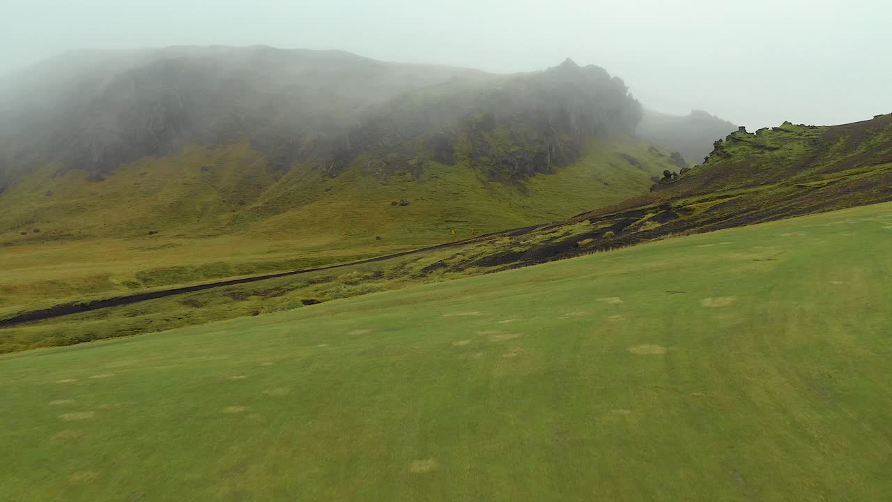 sobrevuelo de campos verdes islandeses con fondo de montañas, paisaje de niebla mística