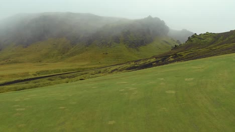 flyover icelandic green fields with mountains background, mystical fog scenery