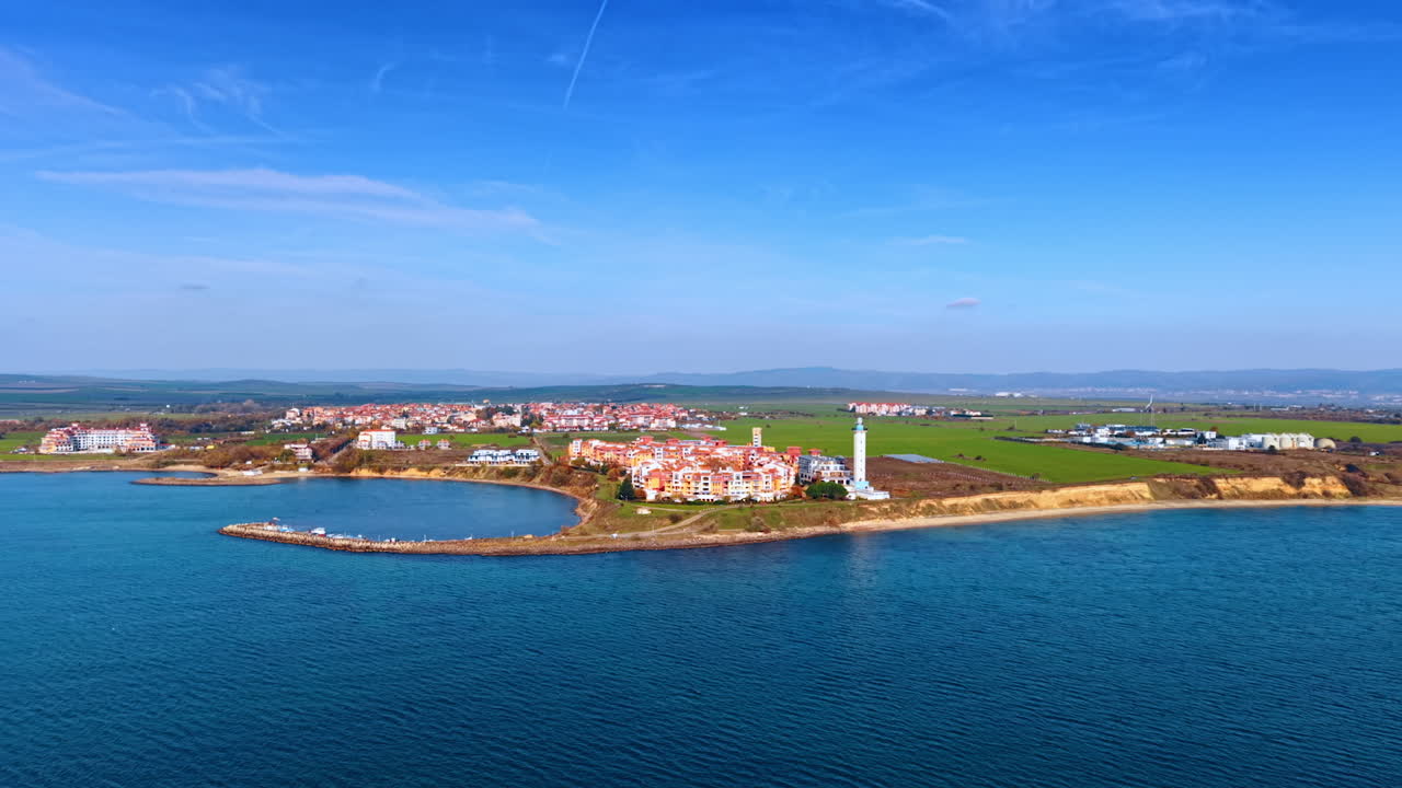 Flight above the blue waterscape of the Black Sea. View on the picturesque city, lighthouse at the coast and long pier