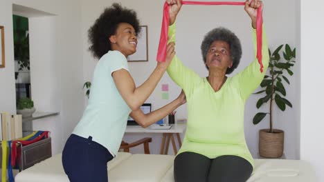 happy african american female physiotherapist helping senior female patient exercise at home