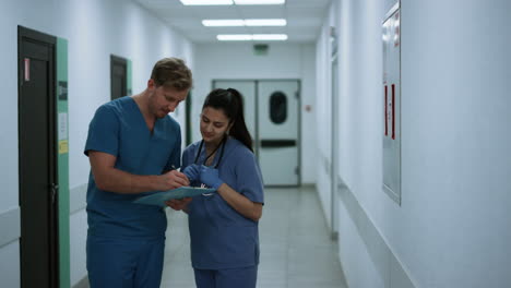 Focused-doctor-discussing-report-with-medical-nurse-in-hospital-corridor.