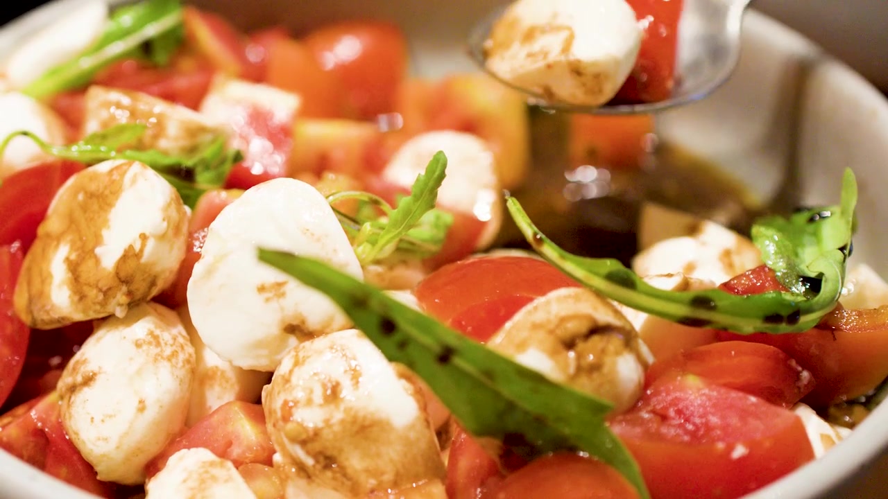 Un cucchiaio di metallo raccoglie insalata caprese fresca con mozzarella, pomodori e glassa balsamica