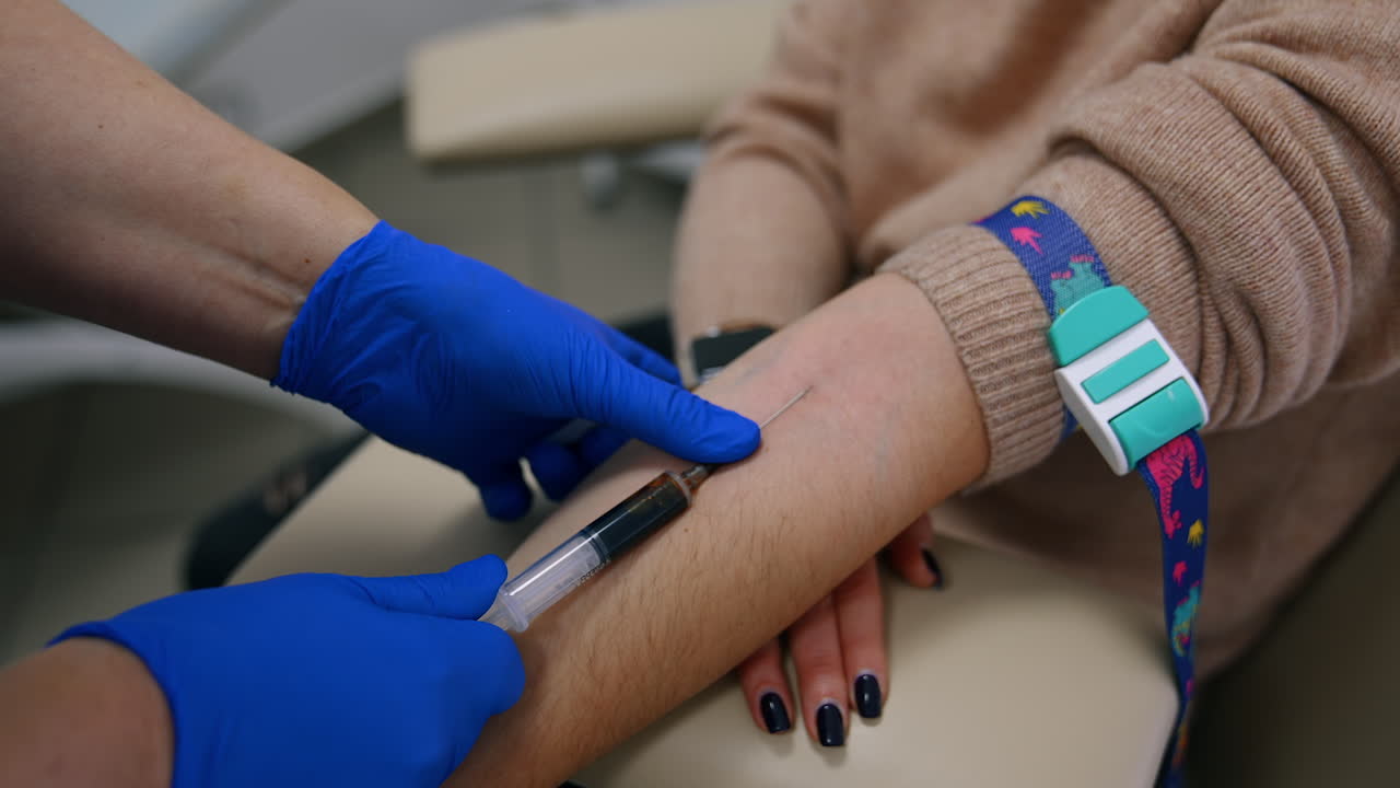 Medic's hands in blue latex gloves fill the syringe with blood. Test sample taking from vein on arm. Close up.