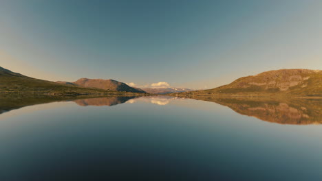 magnificent mountain range perfectly reflected on the tranquil lake water in norway under the clear blue sky - wide drone shot