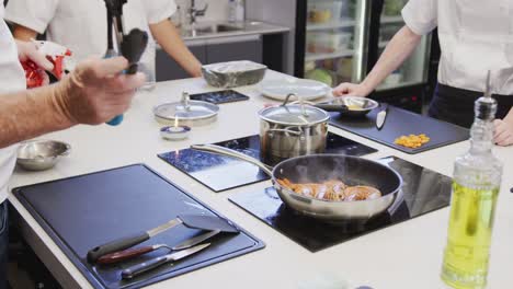 professional caucasian male chef in a restaurant kitchen preparing shrimps using a frying pan