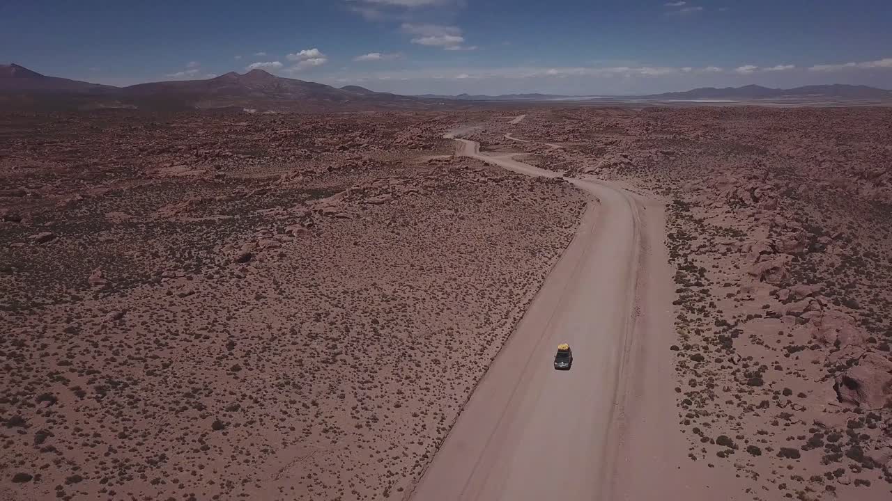 Aerial view of a 4x4 on a dusty red road at the Eduardo Avaroa National Andean Wildlife Reserve, slowly lifting the view to open up to the valley of rocks, "Valle de Rocas" in Uyuni, Bolivia