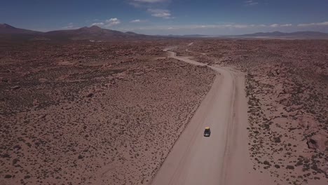 aerial view of a 4x4 on a dusty red road at the eduardo avaroa national andean wildlife reserve, slowly lifting the view to open up to the valley of rocks, "valle de rocas" in uyuni, bolivia