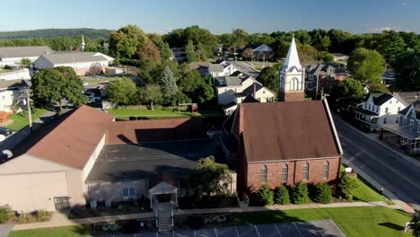 establishing shot of old brown stone, brick lutheran christian church in united states, colonial historic homes line the street during summer aerial scene