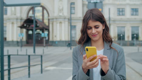 young woman using smartphone and smiling outdoors in city