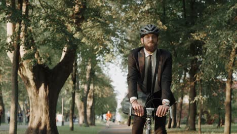 businessman riding a bike in city park wearing suit and helmet, front view