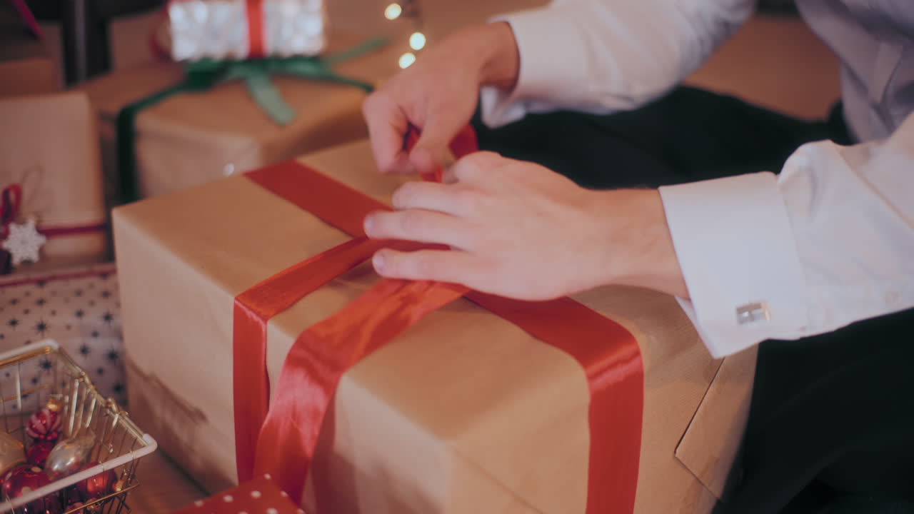Uomo che annoda un nastro rosso su un regalo di Natale incartato