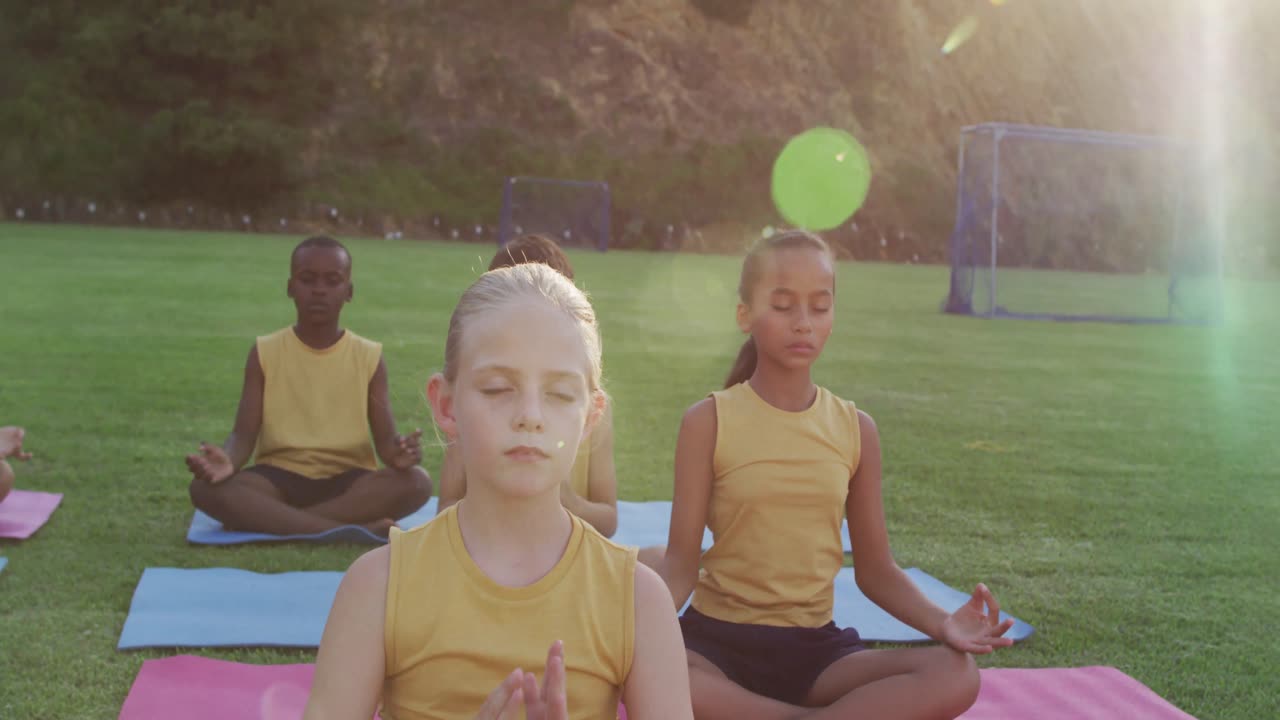 grupo diverso de escolares sentados en esteras meditando durante una lección de yoga al aire libre