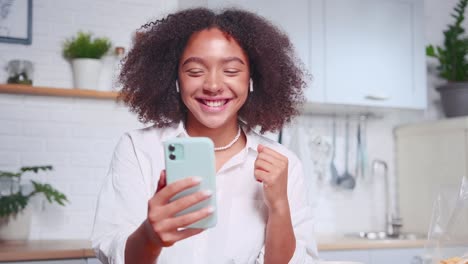 young african american woman makes video call in mobile phone in own kitchen