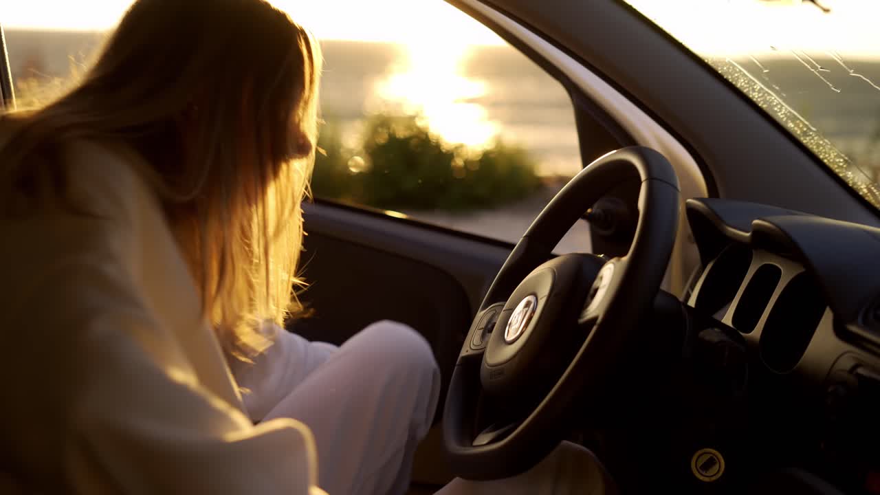 mujer rubia entrando en el coche y arrancando el coche en la costa durante la hora dorada