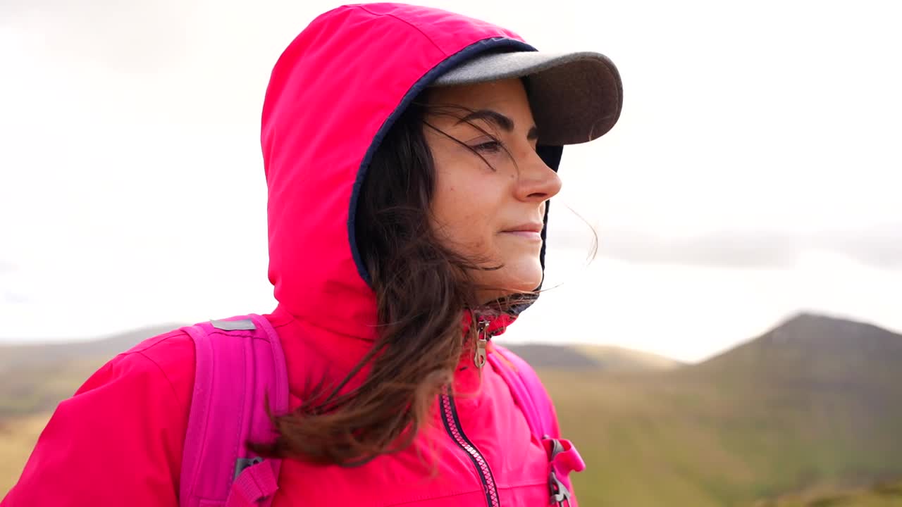 Profile of a hiker in the Welsh hills wearing pink jacket and a cap on windy day