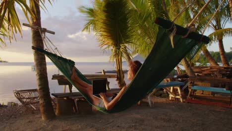 woman working with laptop relaxing on hammock on the beach. concept of digital nomad, remote worker, independent location entrepreneur