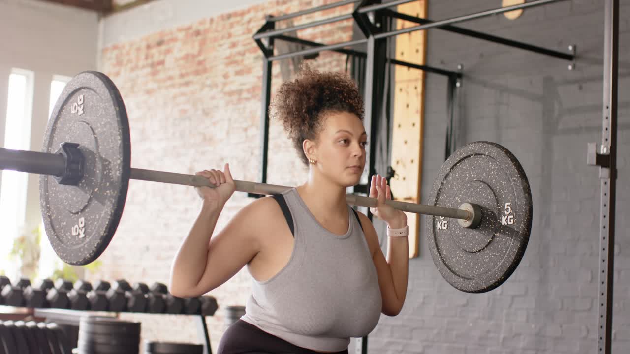 Stepping off rack initiating African American woman repeating barbell squats in gym toning legs