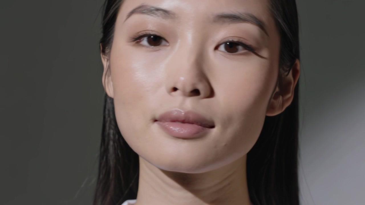 Cahaya studio mengarahkan model Asia berkaus putih berpose dengan latar belakang abu-abu yang berputar menampilkan berbagai sudut wajah.