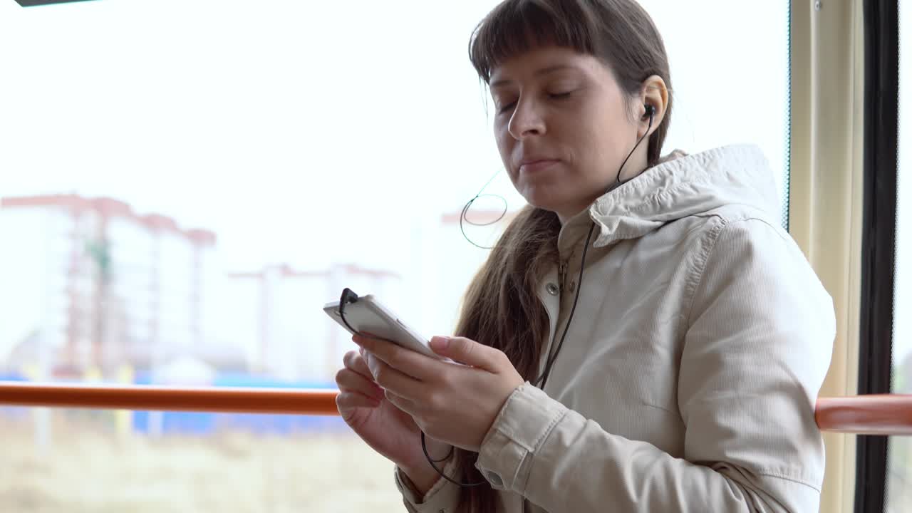 una mujer va en tranvía y escucha música con auriculares en un teléfono inteligente.