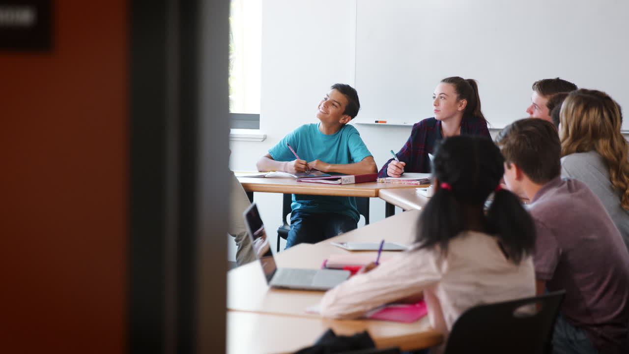 vista a través de la puerta del tutor de la escuela secundaria sentado en el escritorio y enseñando clase