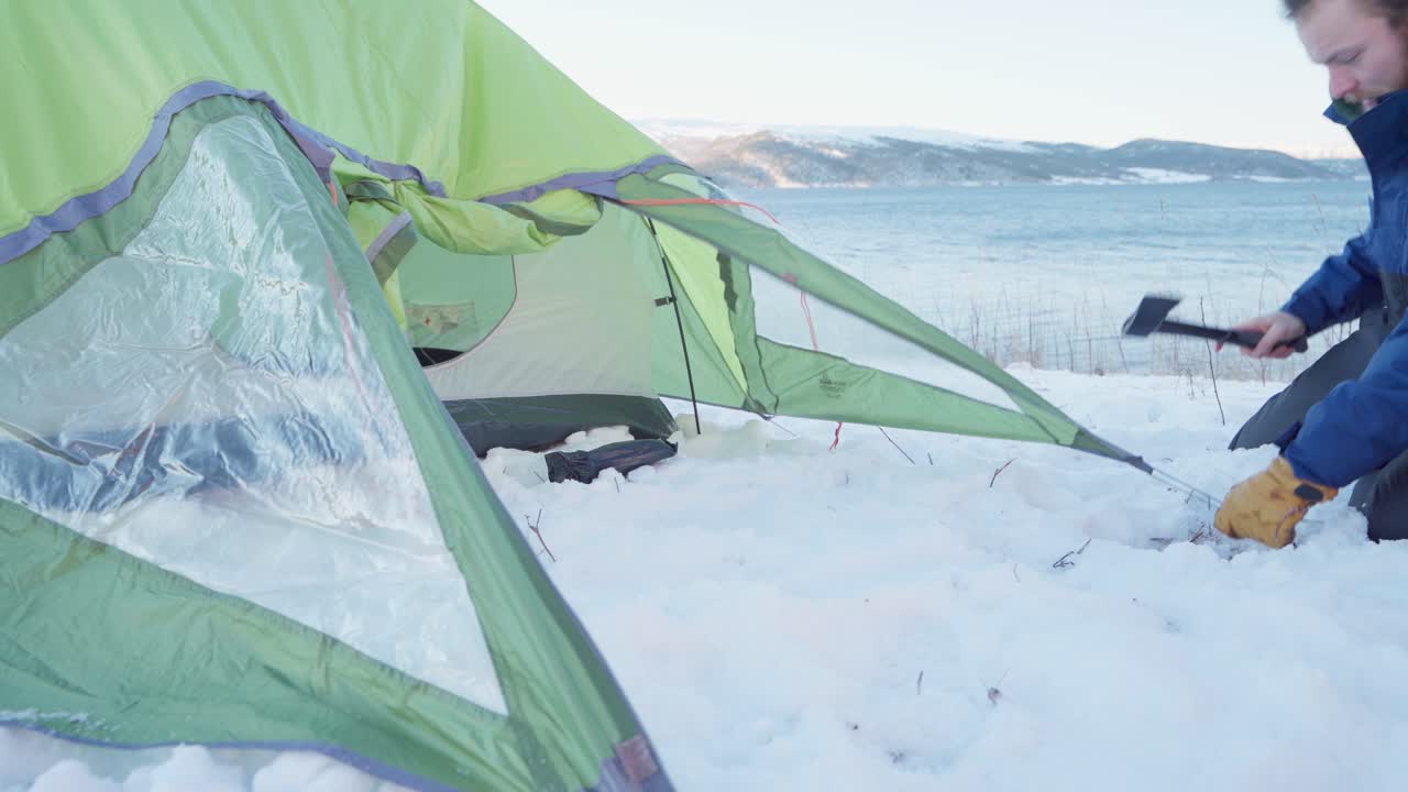 눈 덮인 땅에 말뚝을 두는 방수 텐트를 짓는 남자