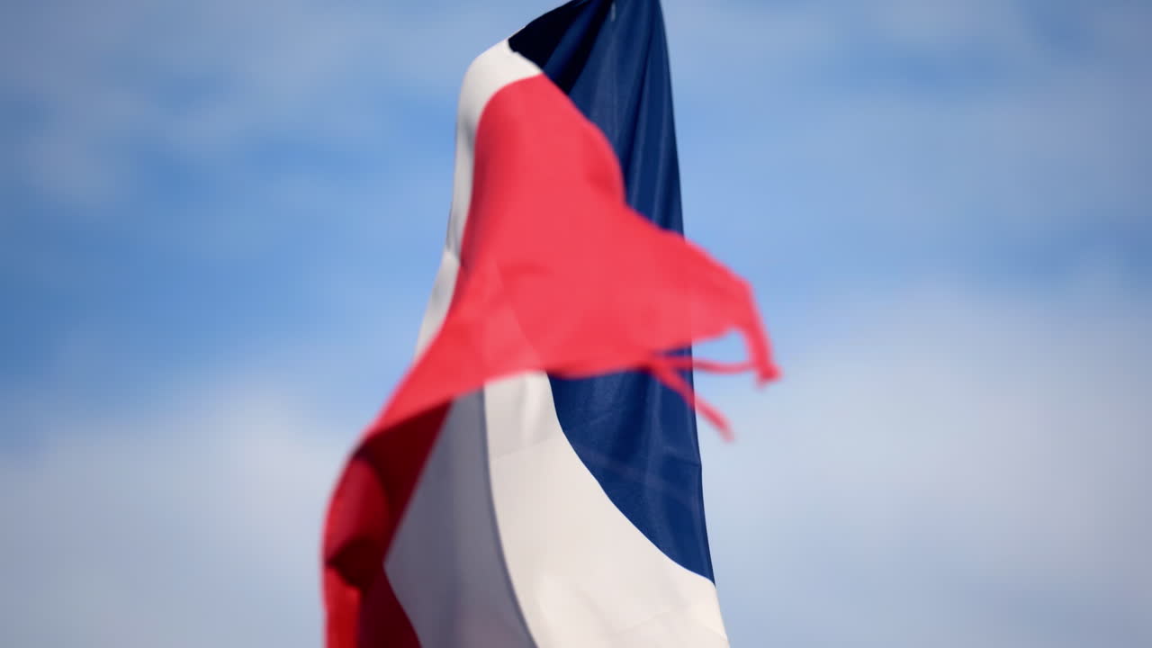 Close up of the flag of France waving in the wind with a blue sky on the background