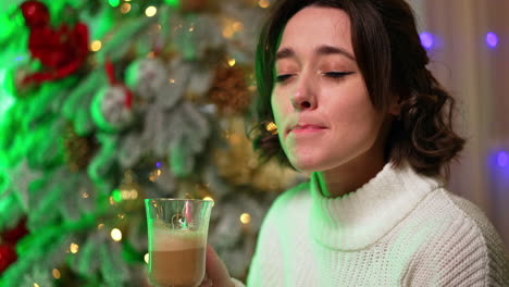 warm drink by the holiday tree. woman sips a cozy beverage in a festive setting with a decorated christmas tree sparkling in the background