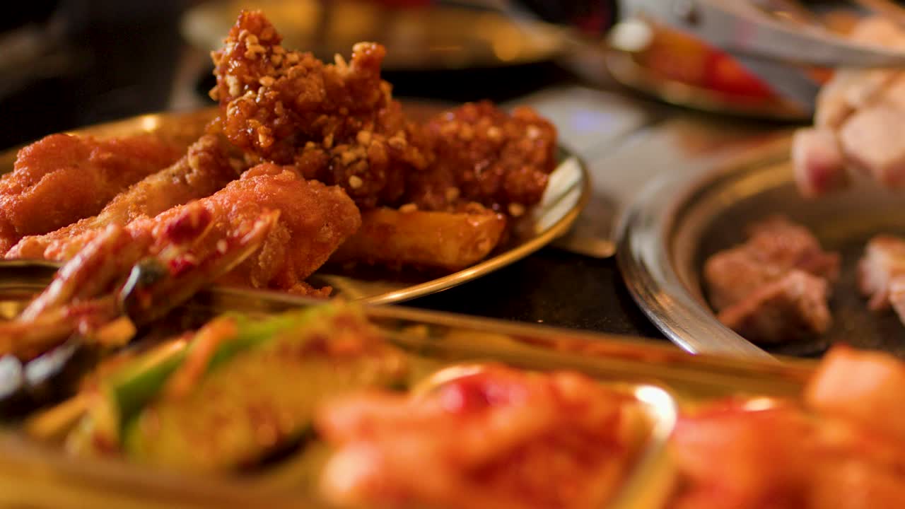 Warm lighting highlights fried chicken, grilled meat, and kimchi at a Korean barbecue restaurant table